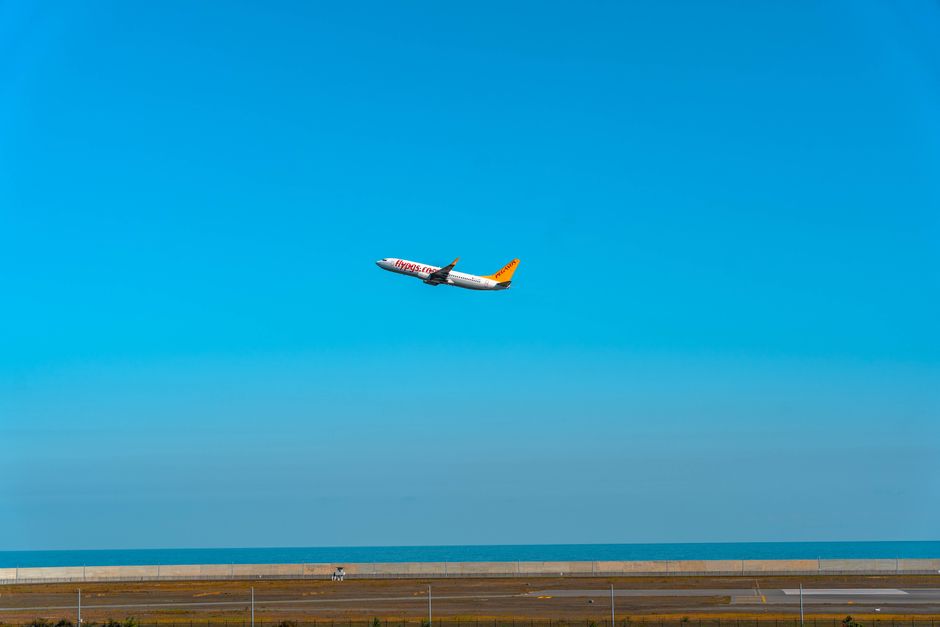 An airplane takes off from an airport runway, soaring into the clear blue sky over the ocean.