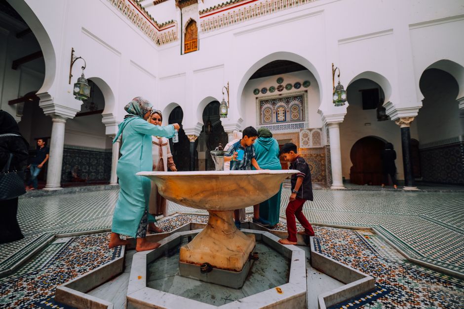 Kids enjoying a fountain in a beautifully tiled courtyard with arched architecture.