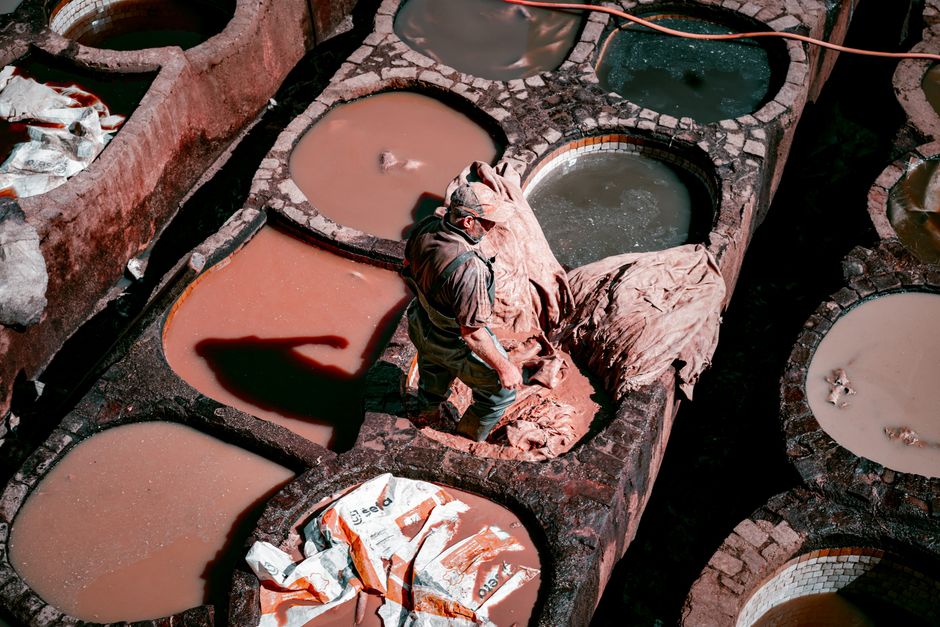 Worker processing leather in an ancient tannery with colorful vats, showcasing traditional methods.