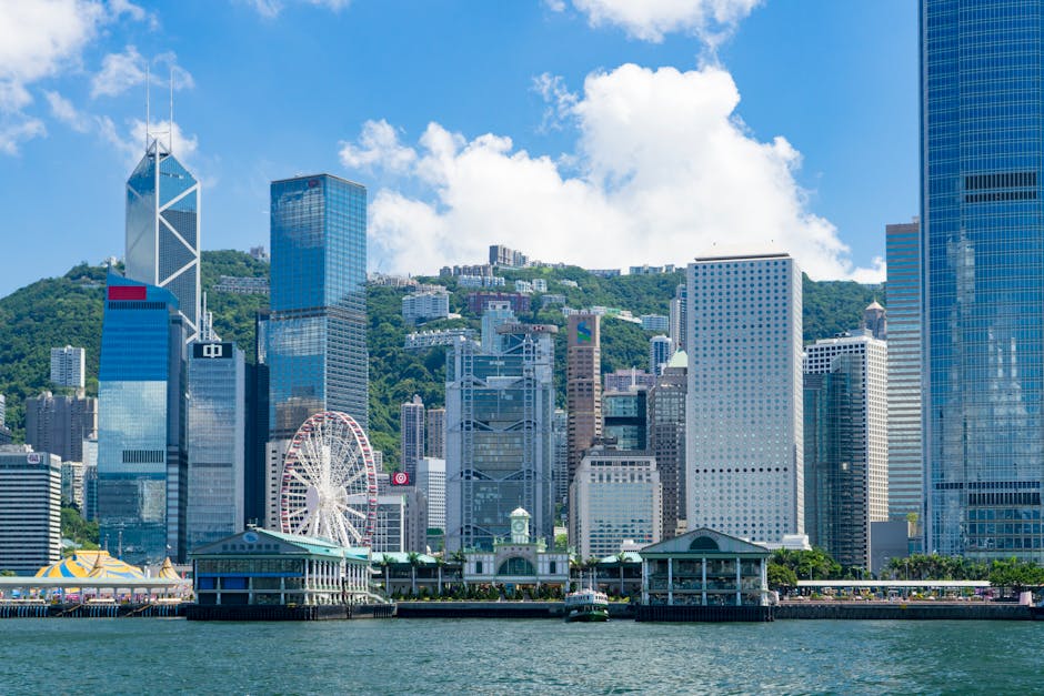 Vibrant view of Hong Kong's modern skyline featuring a ferris wheel and waterfront, under a clear sky.