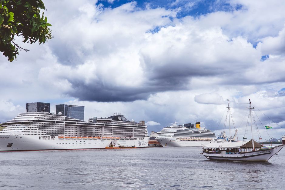 Two grand cruise ships anchored at a vibrant harbor under a dramatic cloudy sky.