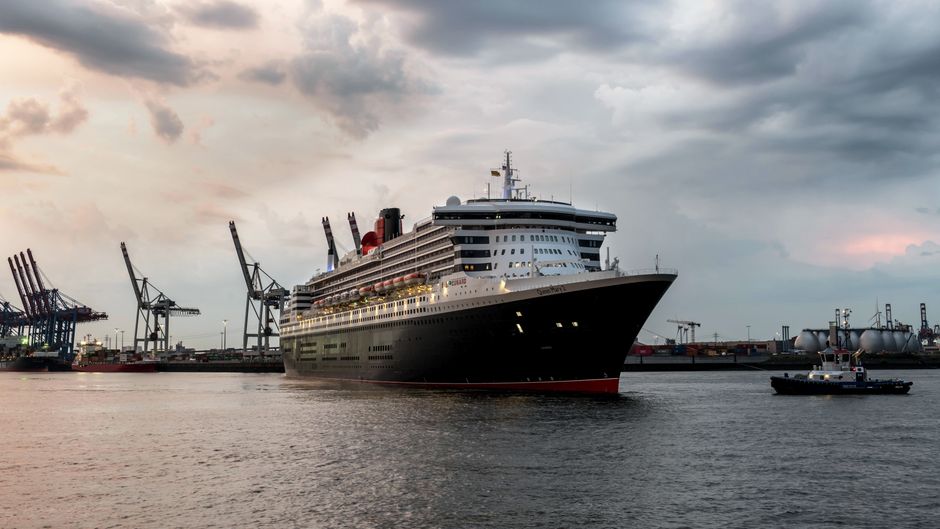 A grand cruise ship navigates Hamburg harbor at sunrise, with industrial cranes in the background.
