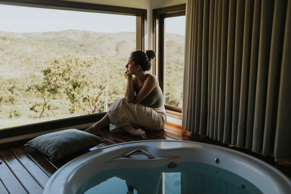Woman gazing through window beside indoor jacuzzi overlooking mountains.