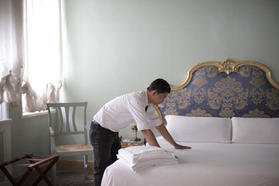 A hotel employee in a luxury room adjusting bed linens, creating a welcoming atmosphere.