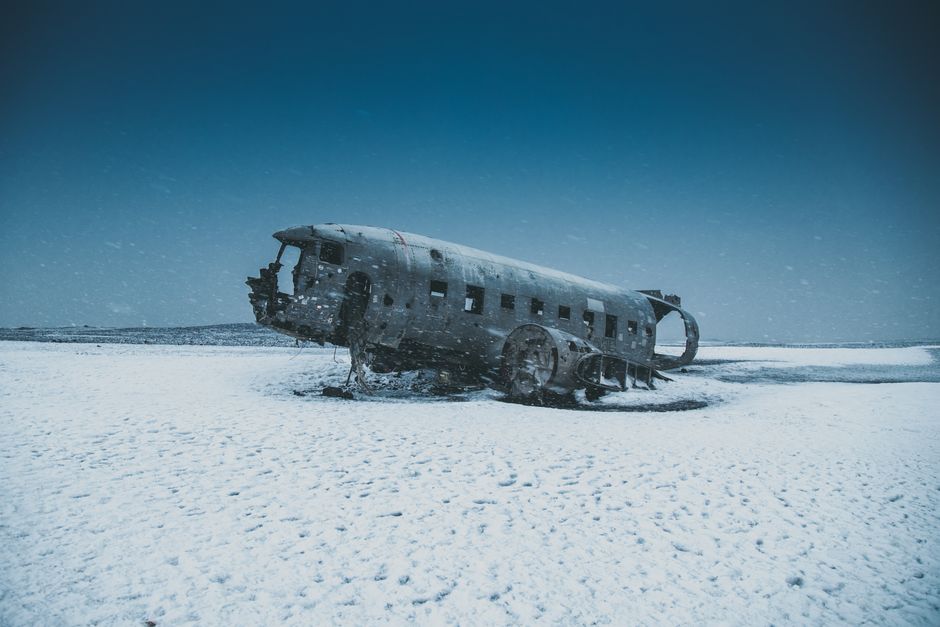 Old abandoned airplane after disaster on snowy terrain behind mounts under sky in winter