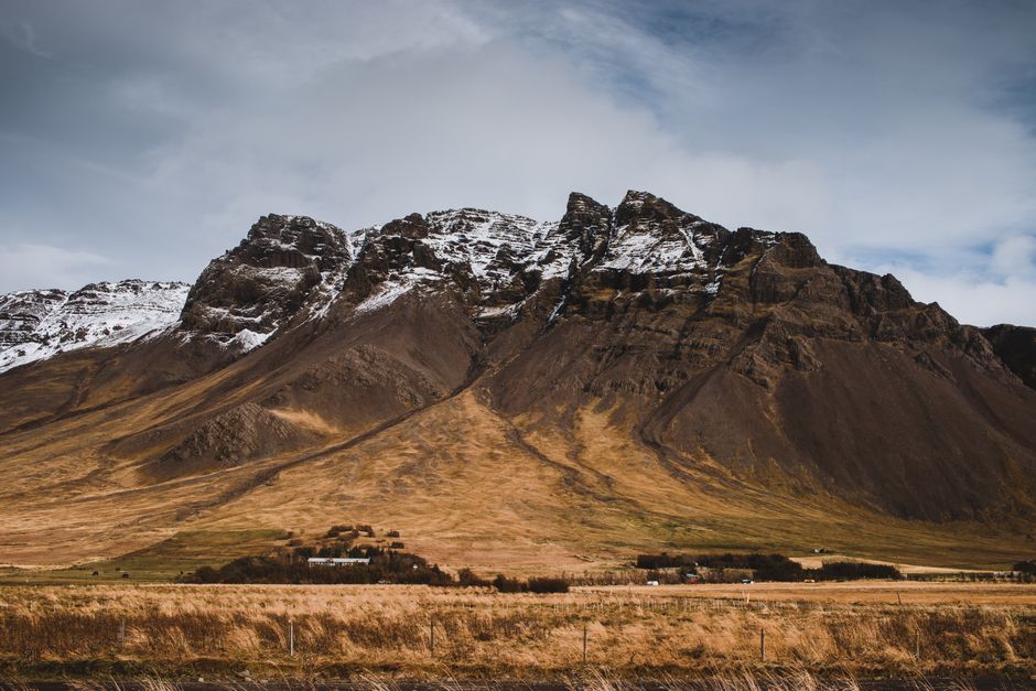 Stunning view of Iceland's rugged mountains with snow caps and autumnal fields below.