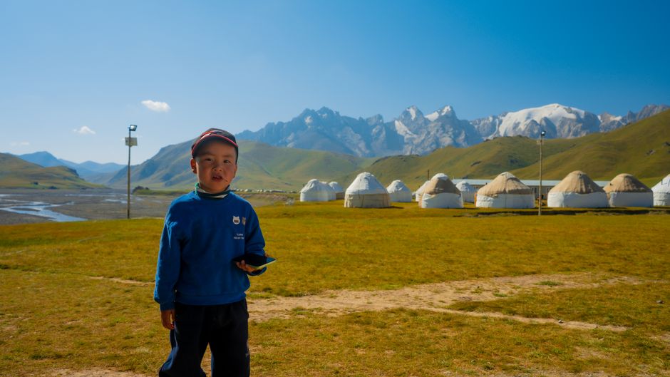 Young boy stands before picturesque yurt village in Kyrgyzstan mountains.