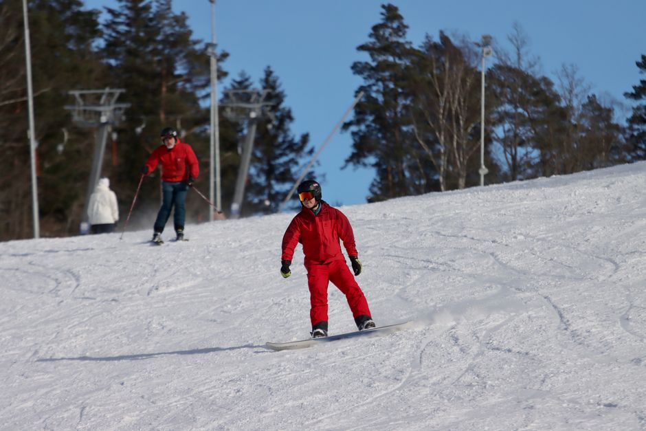 Winter sports enthusiasts skiing and snowboarding on a sunny day in Jönköping, Sweden.
