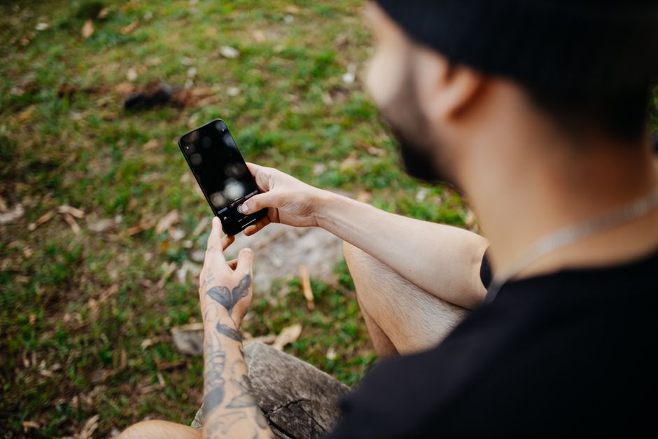 A tattooed man using a smartphone outdoors, demonstrating technology and connectivity.