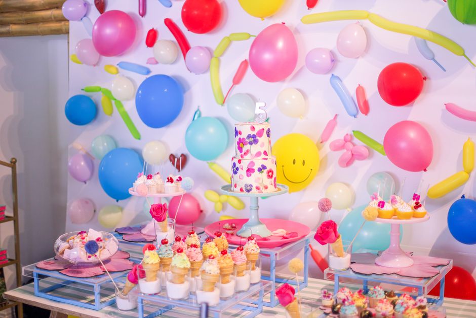 Colorful birthday dessert table with balloons and cake in festive setting.