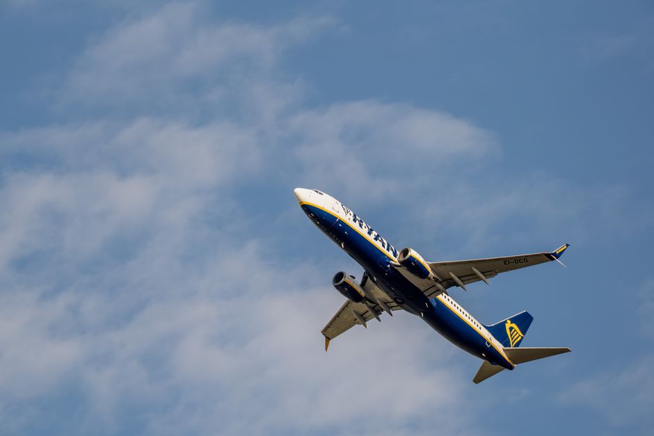 A commercial airplane soars through a bright blue sky with wispy clouds, captured from below.