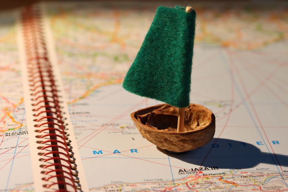 Miniature boat with green sail made from walnut shell on a world map, symbolizing travel and adventure.