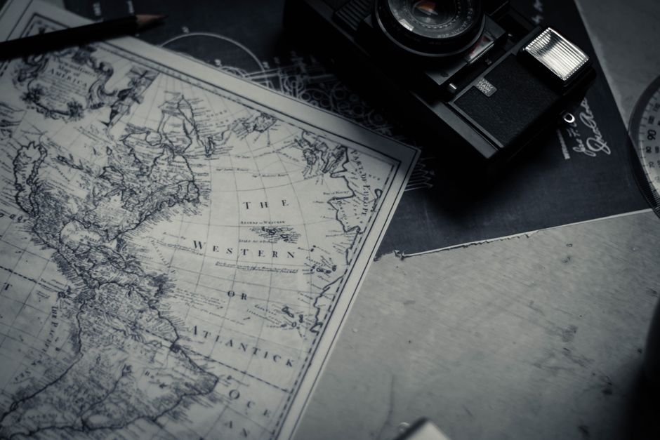 Black and white vintage photo camera and paper map composing with pen and protractor on table in bright room