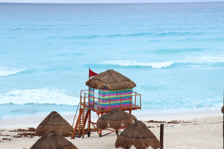 Vibrant lifeguard tower on Cancún's sandy beach, set against turquoise ocean waves.