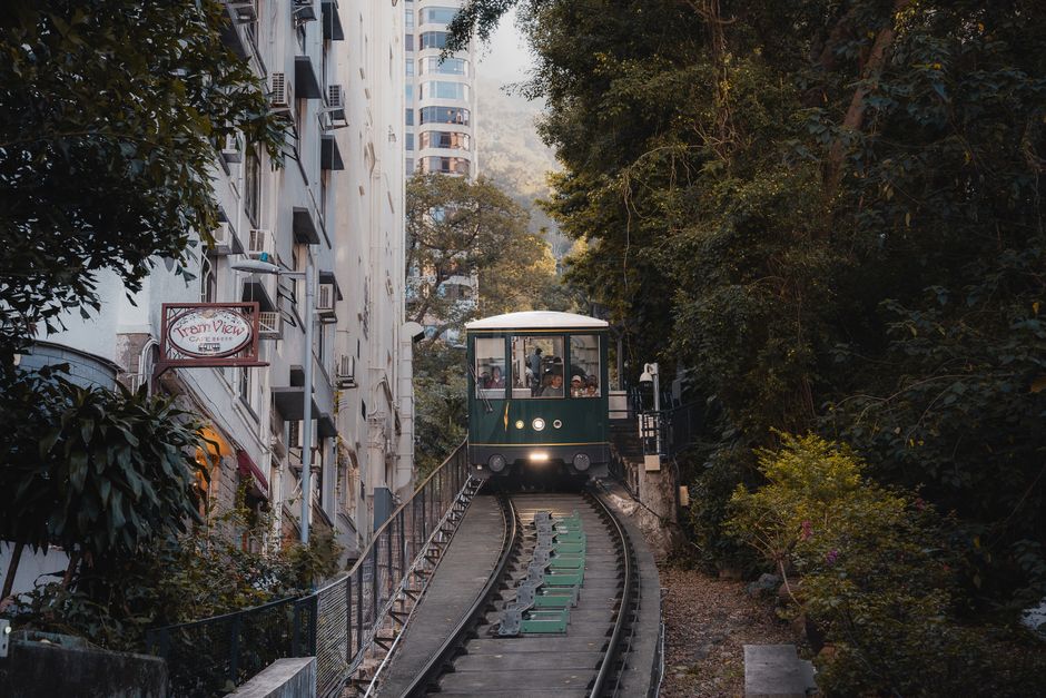 Scenic view of Hong Kong tram climbing forested hillside, blending urban and natural elements.