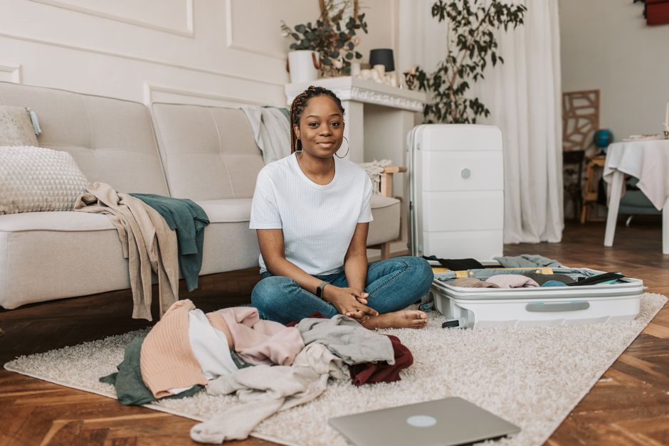 Young woman sitting on rug in living room, packing suitcase for travel.